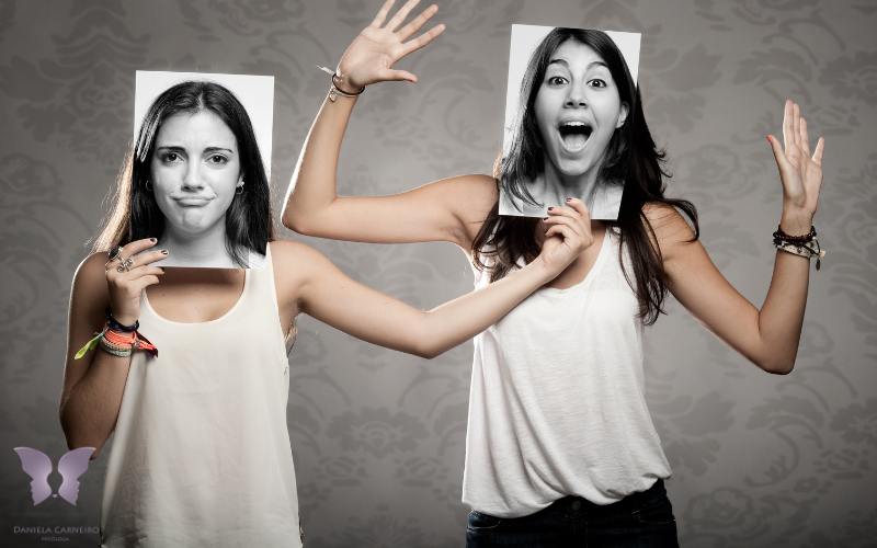 Mulheres segurando máscaras com expressões faciais contrastantes.